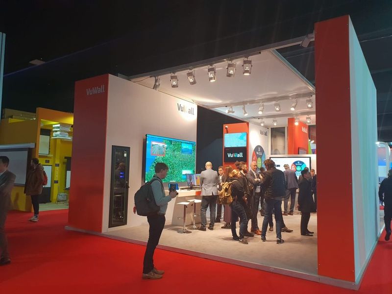 Stand van VuWall met rode wanden en bezoekers voor een schermenwand